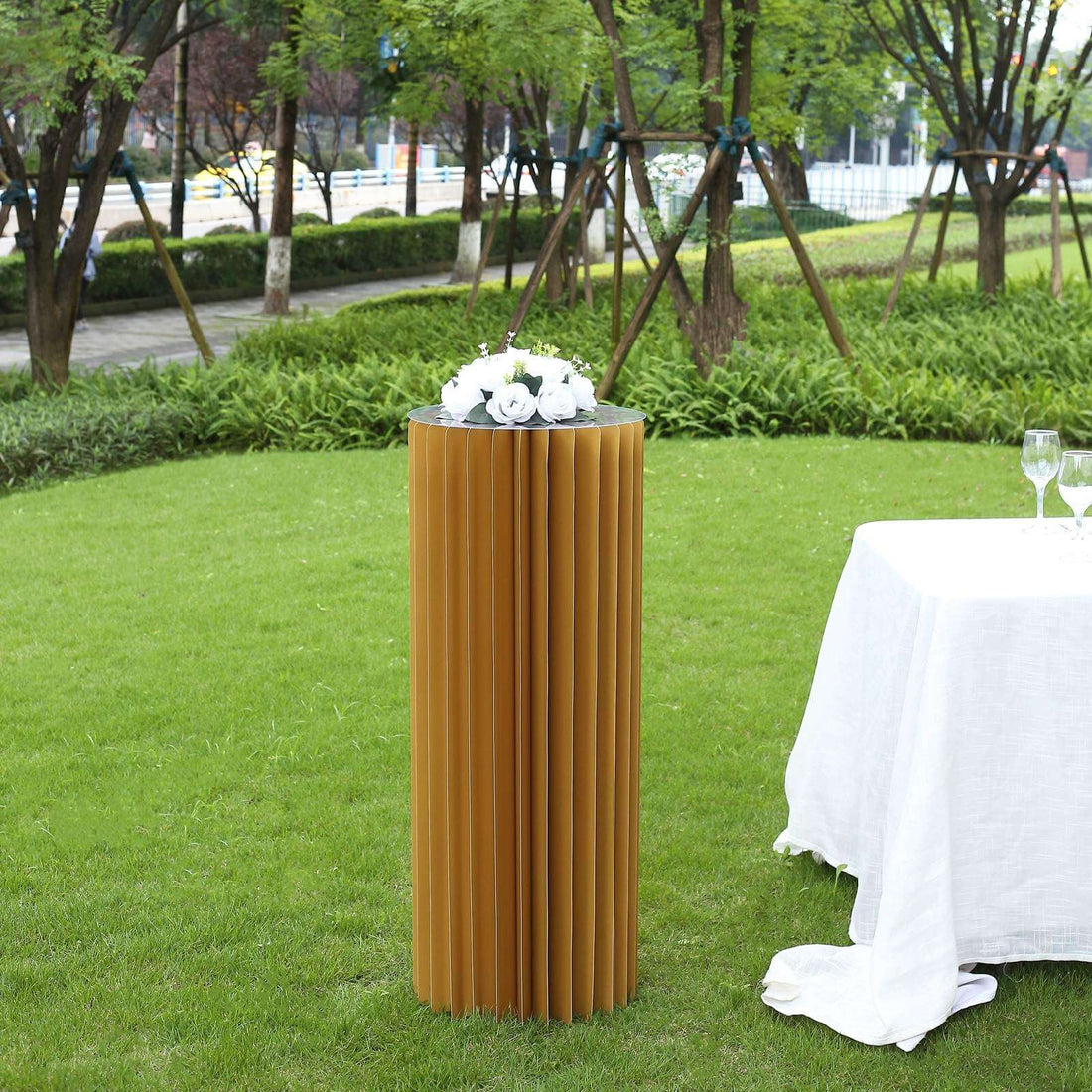 Elegant cylindrical table with flowers, set in a lush outdoor garden scene.