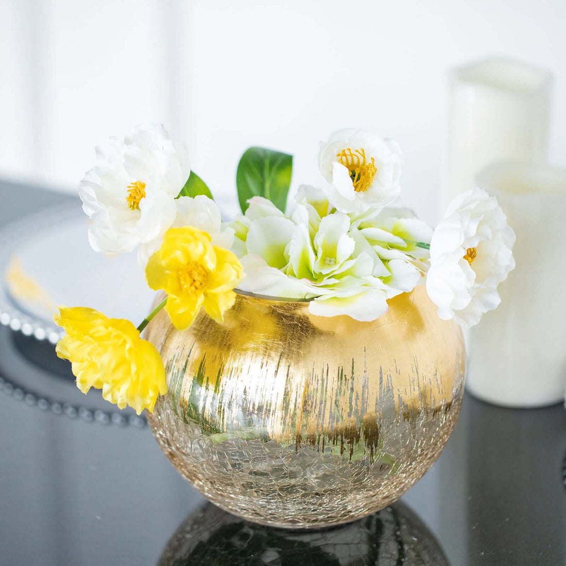 Gold vase with white and yellow flowers arranged elegantly.