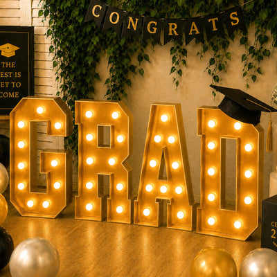 Gold graduation letters “GRAD” with lights and cap at celebration backdrop