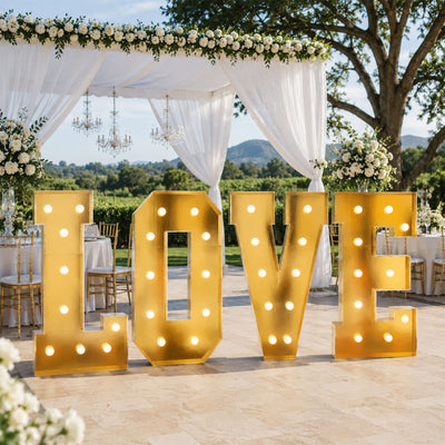 Gold illuminated LOVE sign at outdoor wedding reception under floral canopy