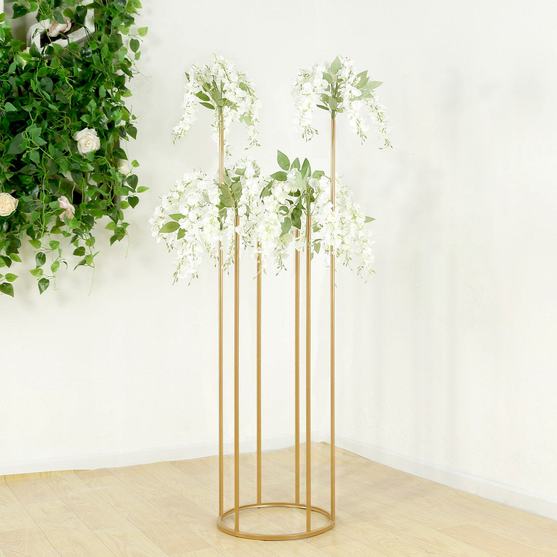 Gold flower stand with white wisteria blooms and green leaves.