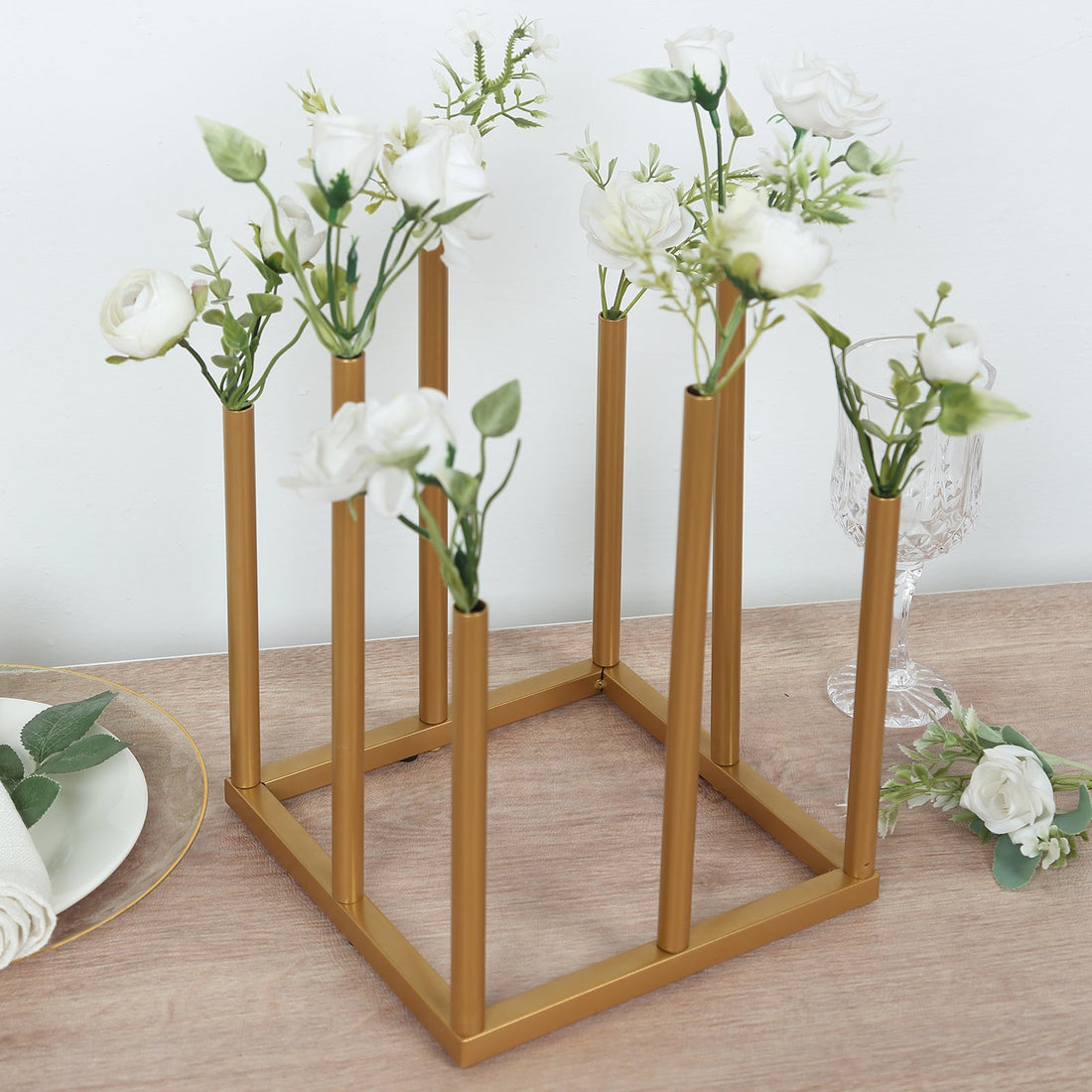Gold flower vase holder with white roses on a wooden table.
