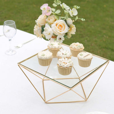 Decorative glass display stand with cupcakes and floral arrangement on a table.