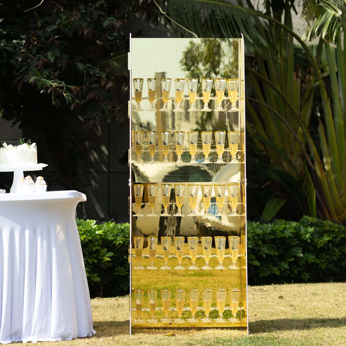 Gold champagne tower display at outdoor event with white table setup.