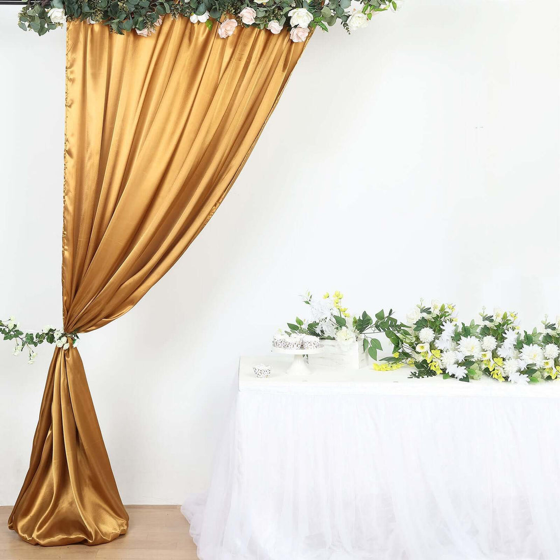 Gold satin curtain with floral accents and white table decor.