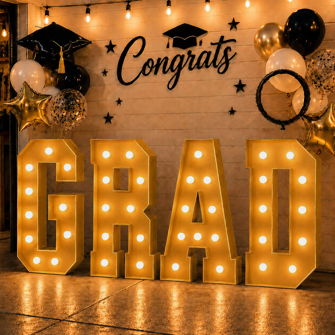 Graduation party backdrop with gold GRA letters and black-and-gold balloons