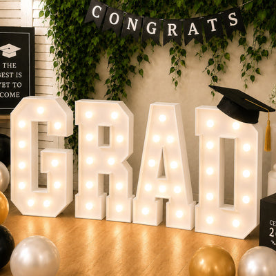 Graduation party decor with lighted “GRAD” letters and cap backdrop