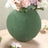 Green round vase with flowers on a wooden table.