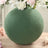 Green round vase with flowers on a wooden table.