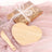 Heart-shaped bamboo serving board with a wooden spoon on a soft pink backdrop.