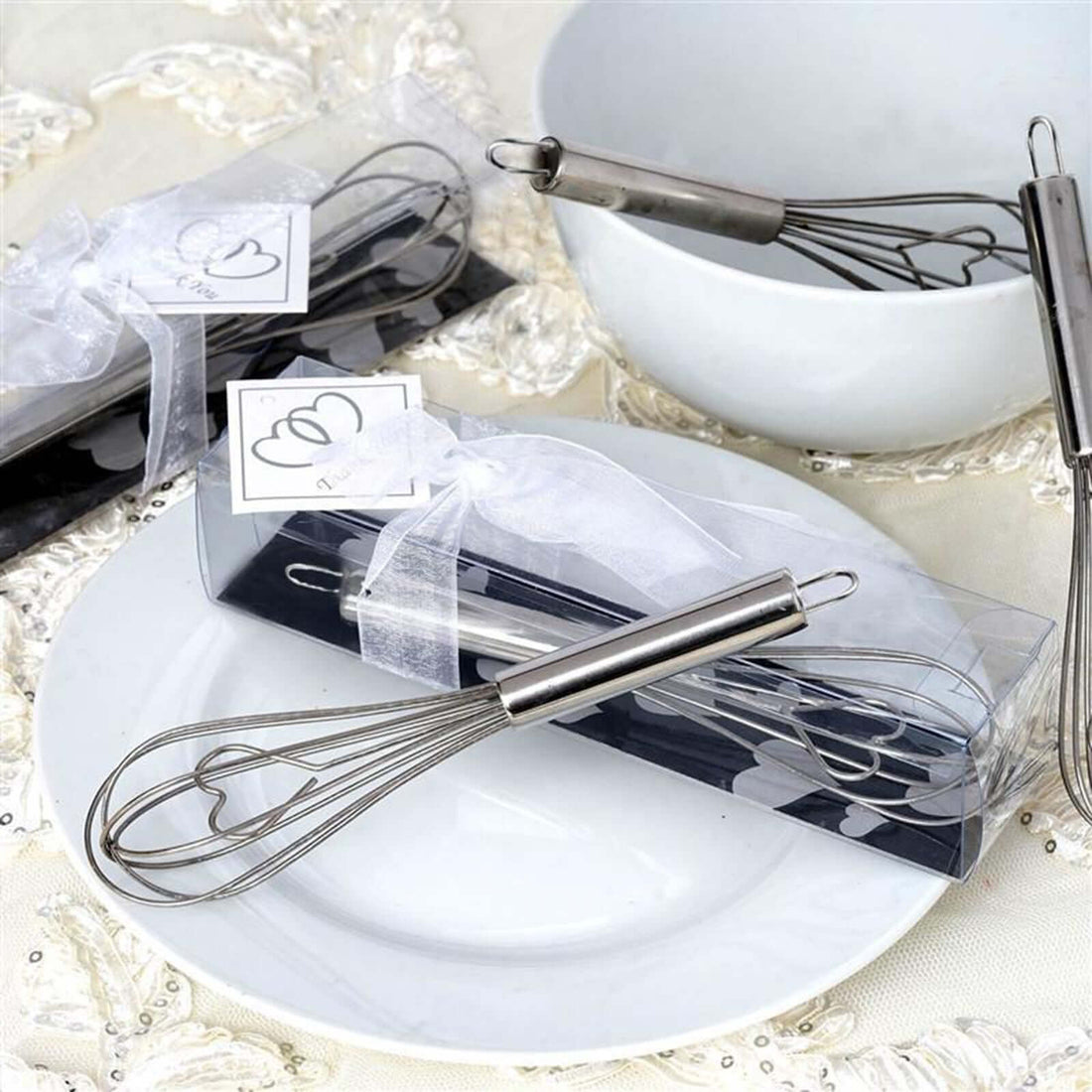 Stainless steel whisk set in packaging with a bowl and plate in the background.