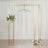 Gold wedding arch with floral arrangements on a soft backdrop.