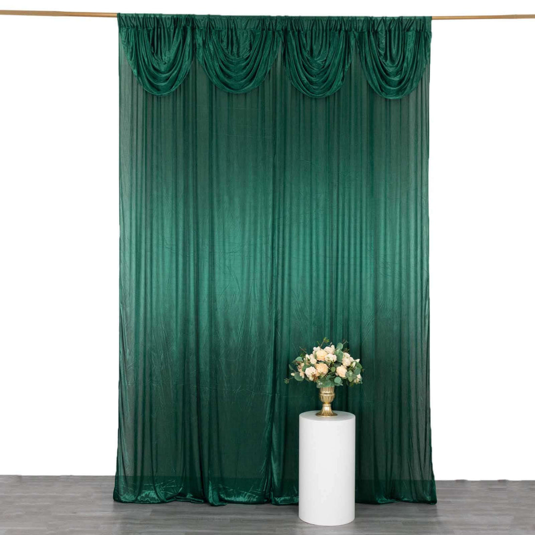 Green draped fabric backdrop with decorative pleats and floral arrangement.