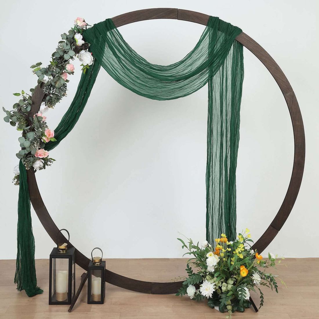 Decorative wedding arch with greenery and flowers, featuring lanterns and draped fabric.