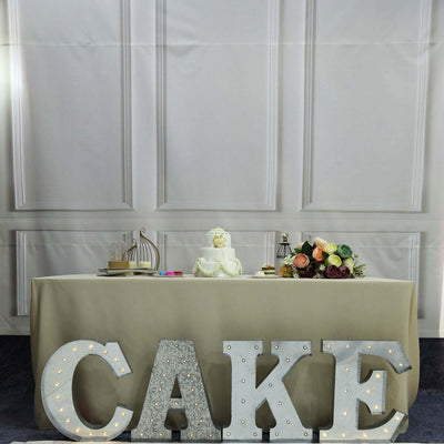 Elegant wedding cake table with floral arrangement and illuminated “CAKE” letters.