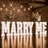 Illuminated MARRY ME wedding proposal sign with floral arrangements in rustic venue
