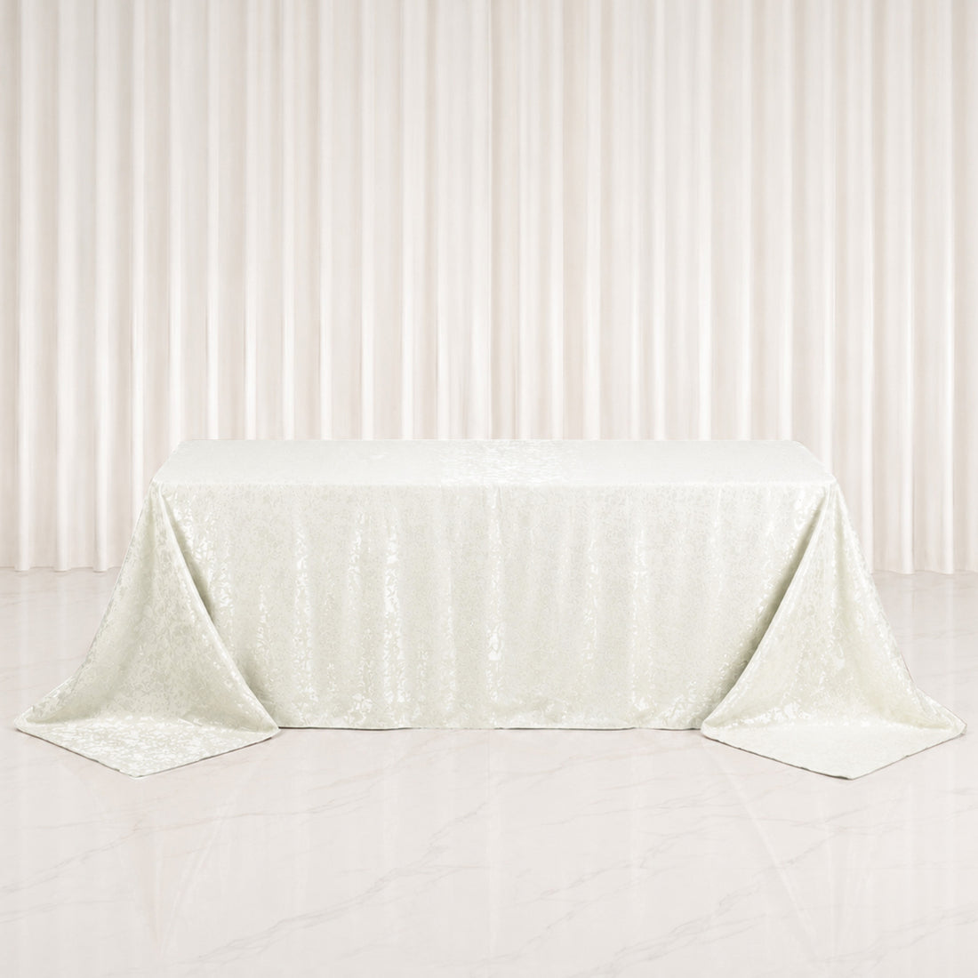 Ivory jacquard tablecloth draped on rectangular table with elegant backdrop