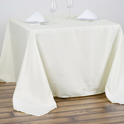 Elegant ivory tablecloth draped on a wooden dining table with glassware.