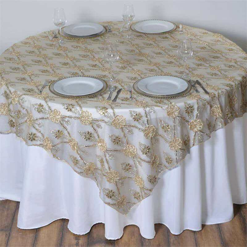 Round table covered with elegant gold floral lace tablecloth and white plates.