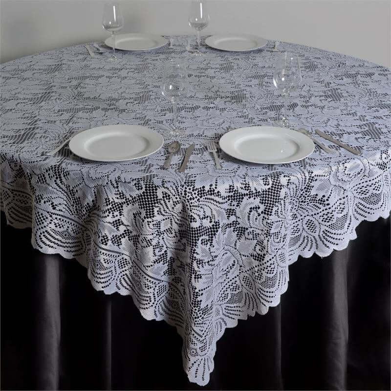 Lace tablecloth draped over a round table set with plates and glasses.