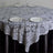 Lace tablecloth draped over a round table set with plates and glasses.