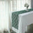 Green lace table runner on a white table with a vase of flowers in a bright room.