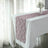 Lace table runner in mauve on a white table with flowers in a vase.