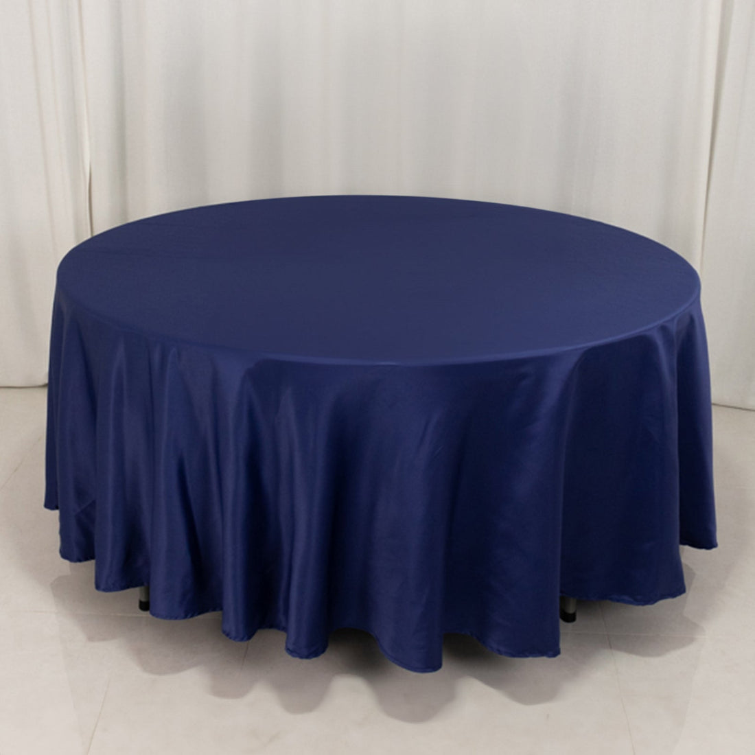 Round navy tablecloth with elegant draping on a plain backdrop.