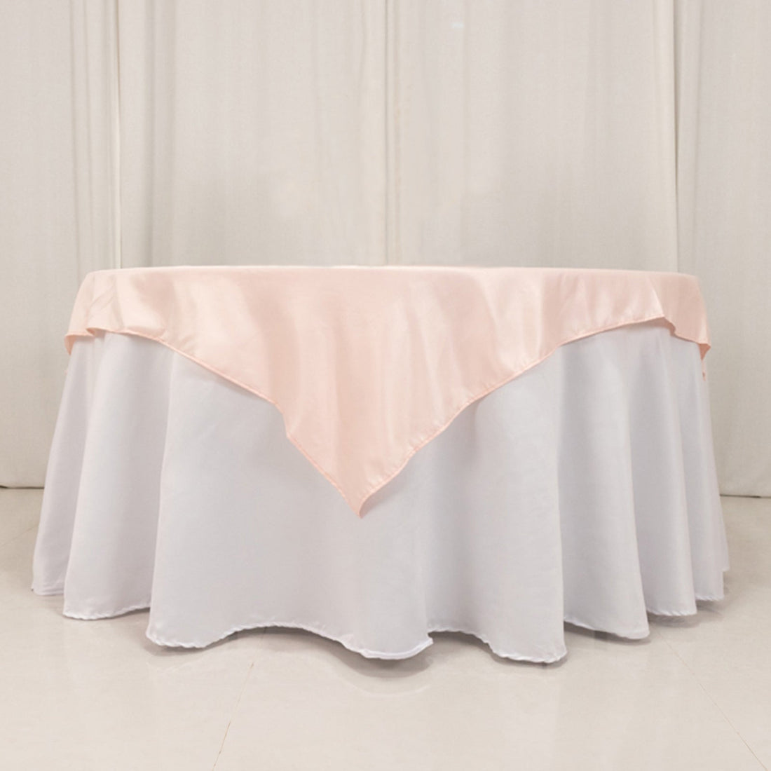 Round table with white tablecloth and pink satin overlay