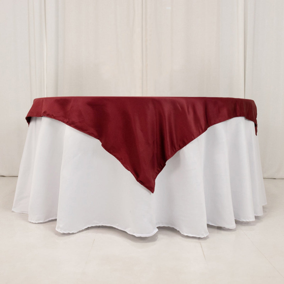 Round table with white tablecloth and burgundy satin overlay