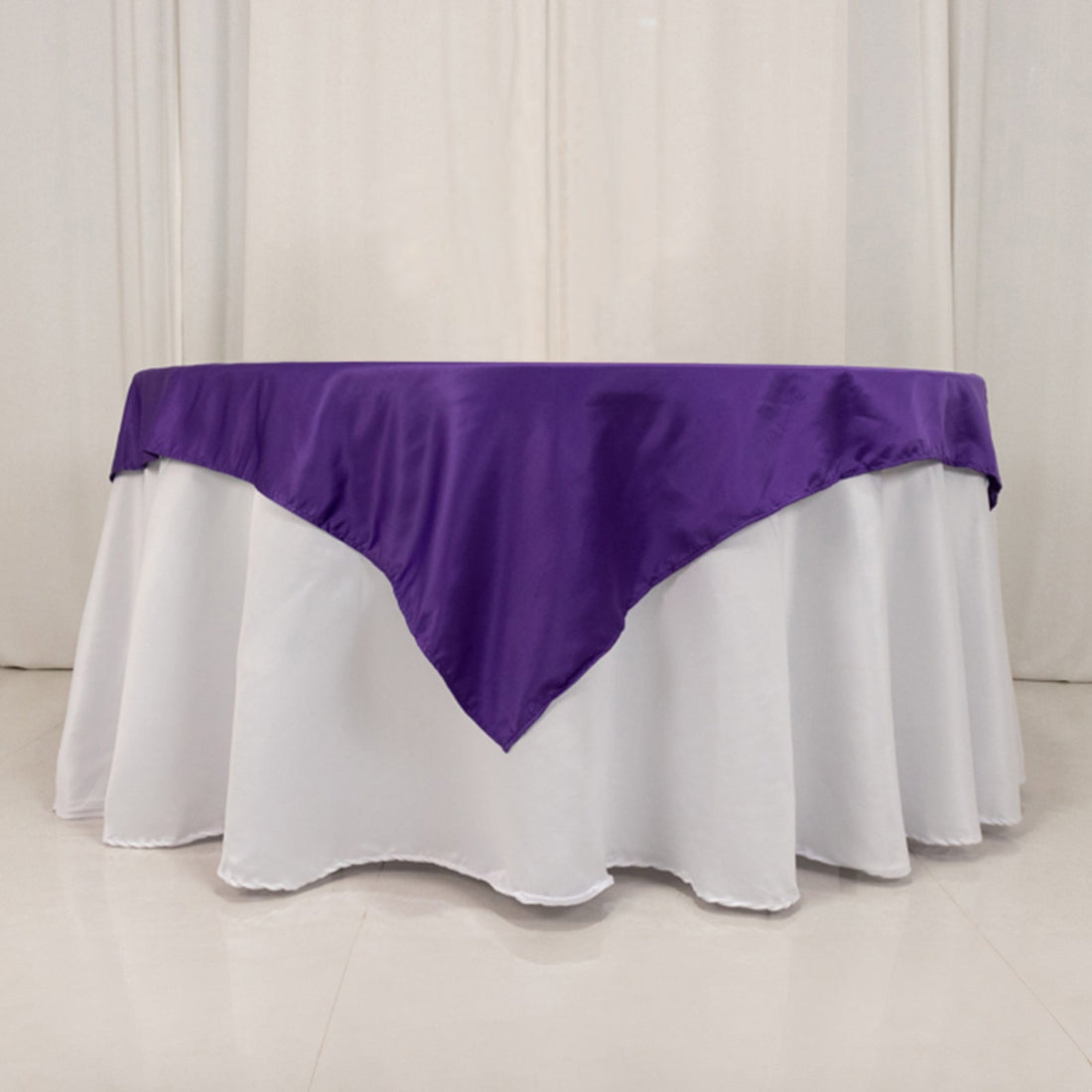 Purple tablecloth draped over a round table with white base.