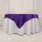 Purple tablecloth draped over a round table with white base.