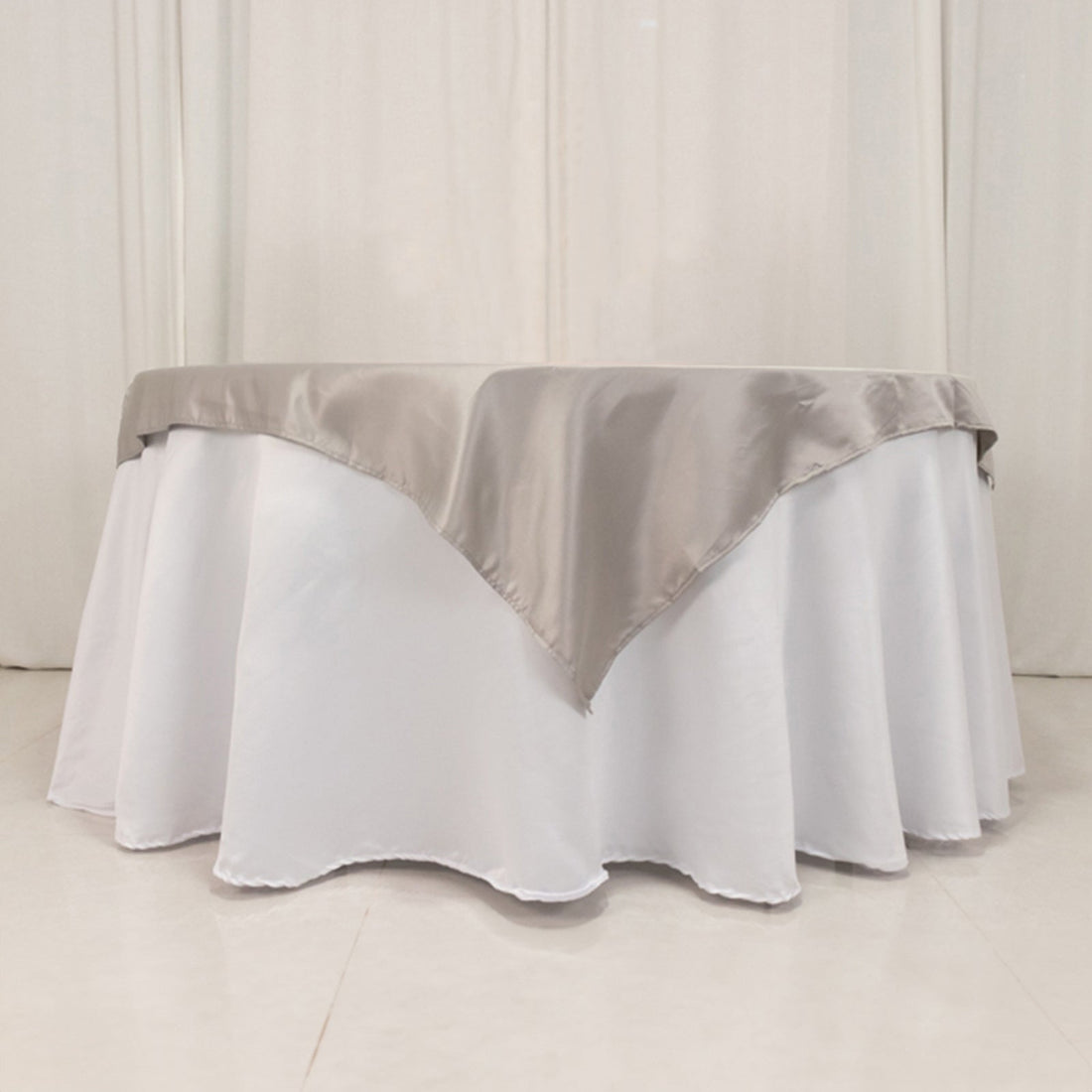 Elegant round table with white tablecloth and silver satin overlay