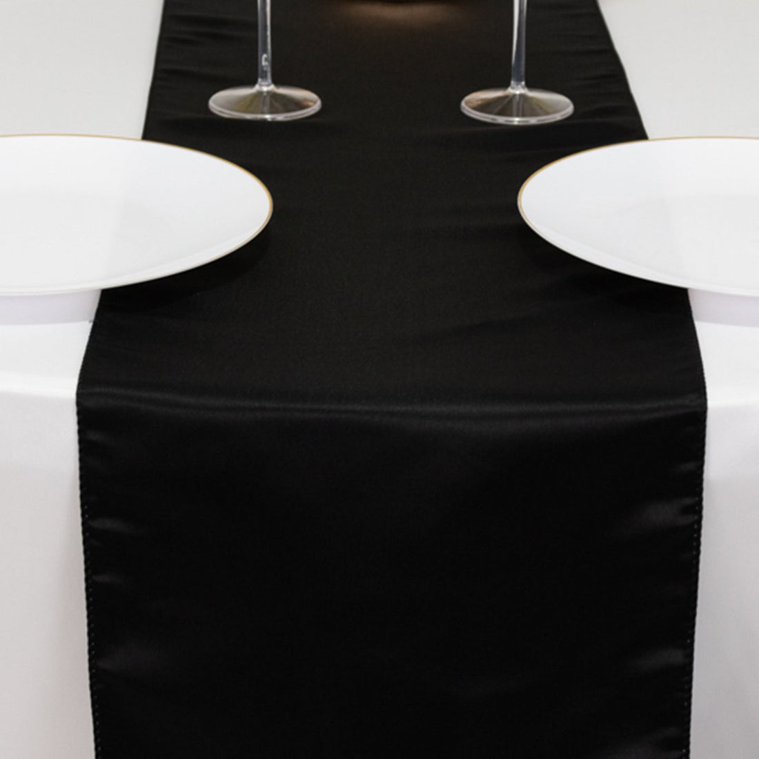 Elegant black satin table runner with white plates and wine glasses.