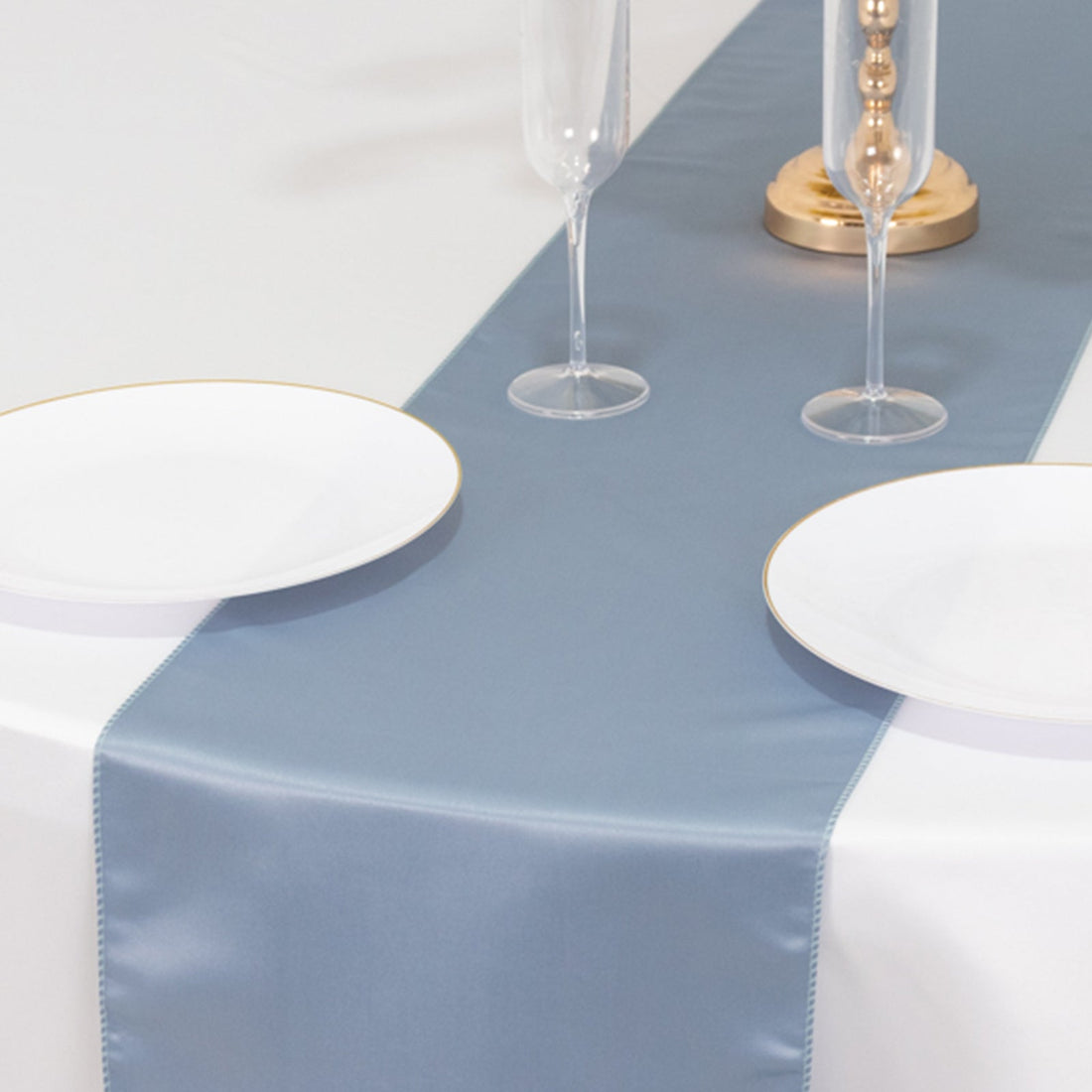 Blue satin table runner on a white table with plates and glasses.