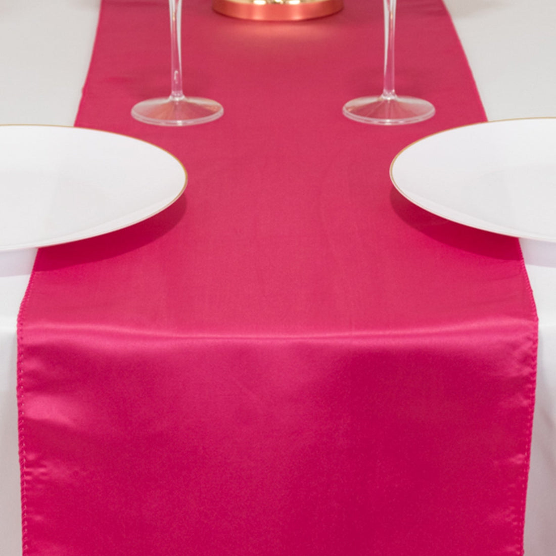 Pink satin table runner on a dining table with plates and glasses.