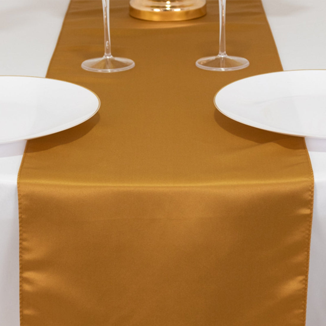 Gold table runner on a dining table with white plates and glasses.