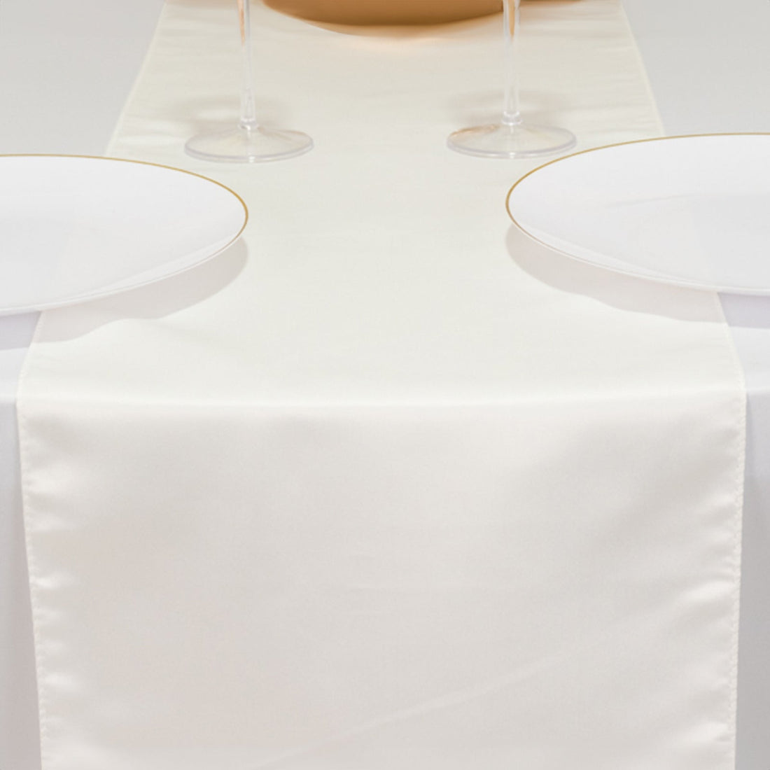 Elegant ivory table runner on a dining table with white plates and glasses.