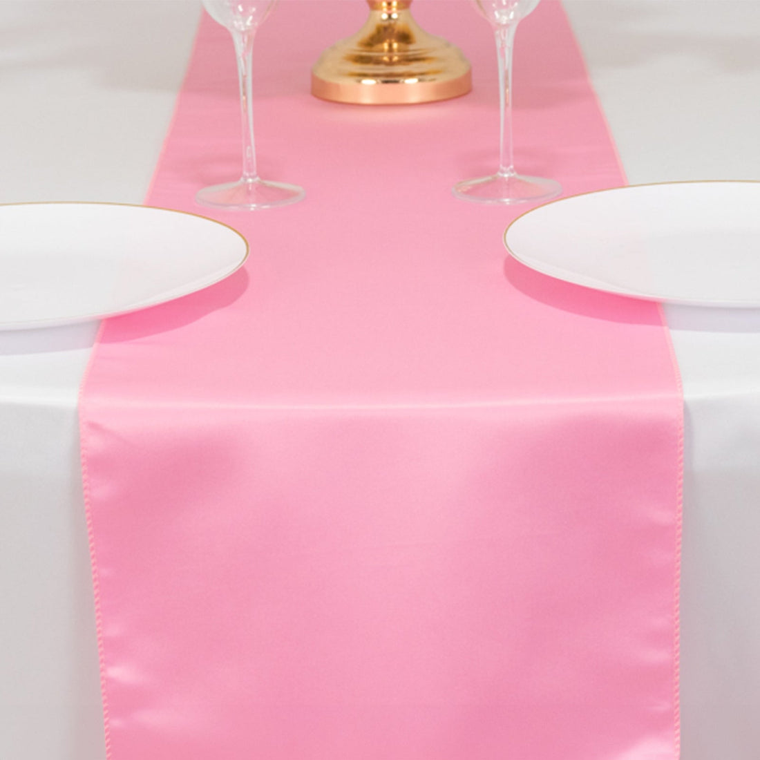 Pink table runner on a white table, set for dining with plates and glasses.
