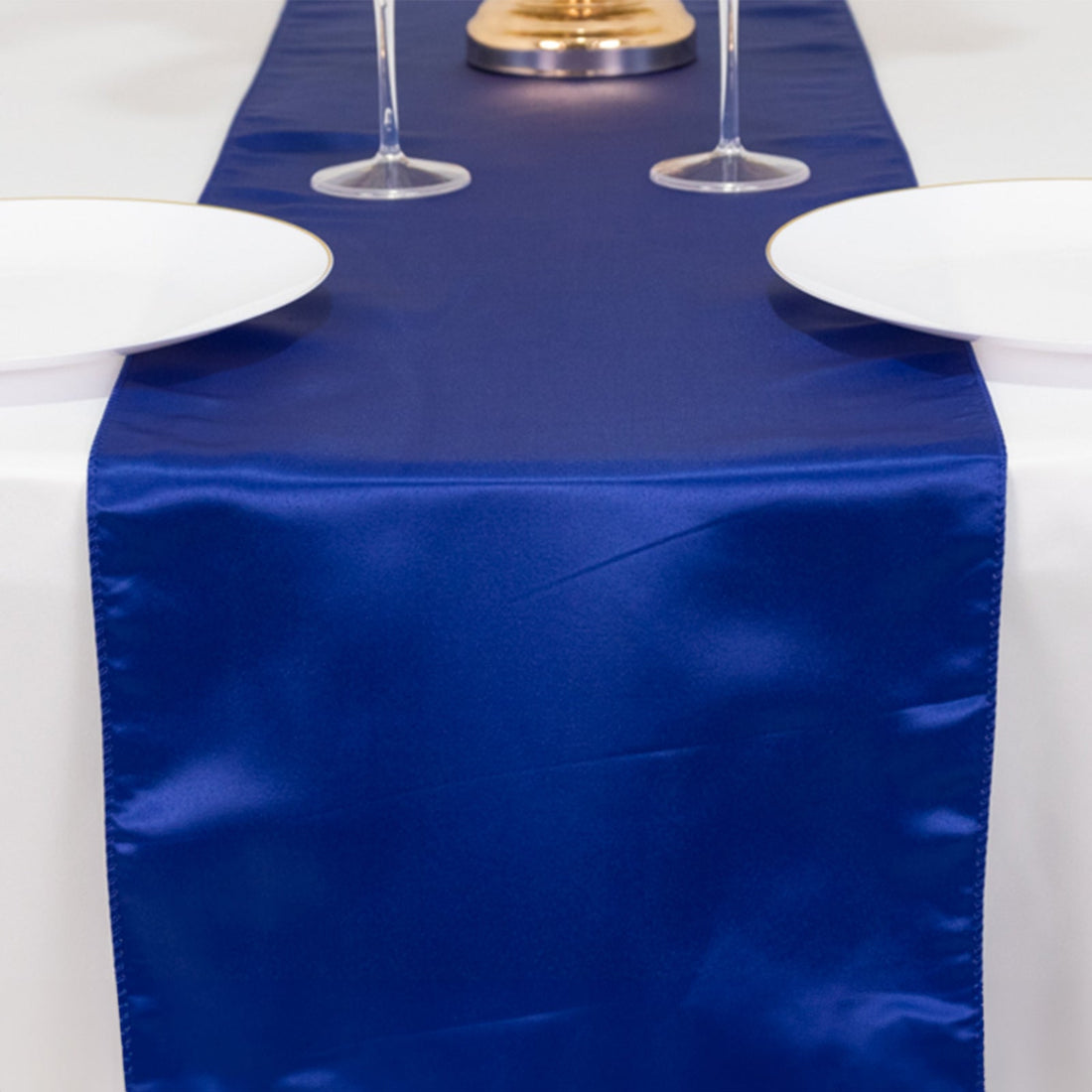 Navy blue satin table runner on a white table with plates and glasses.