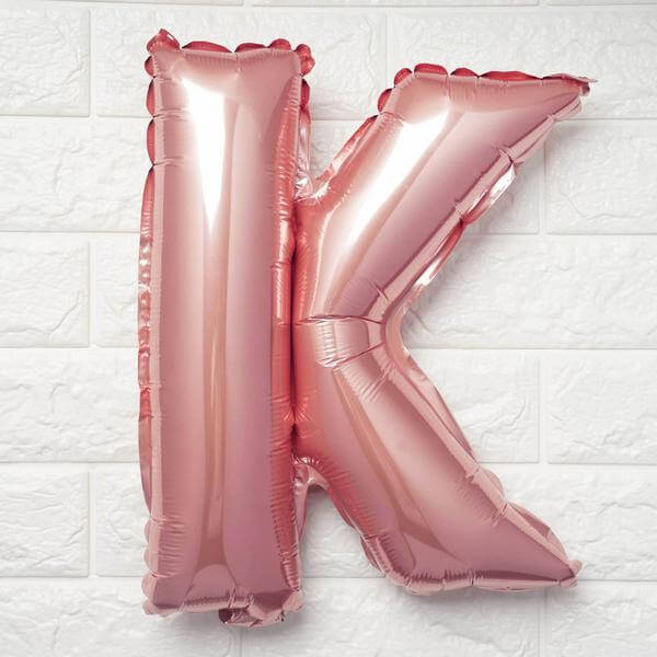 Rose gold letter K balloon against a textured white wall.