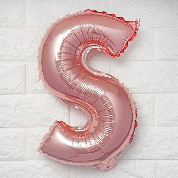 Rose gold letter S balloon on a textured white wall.