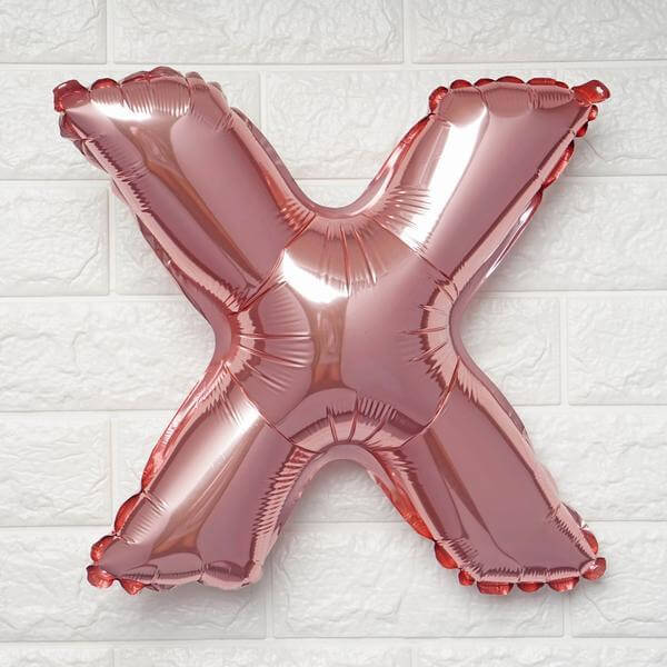 Rose gold X balloon on a textured white wall.