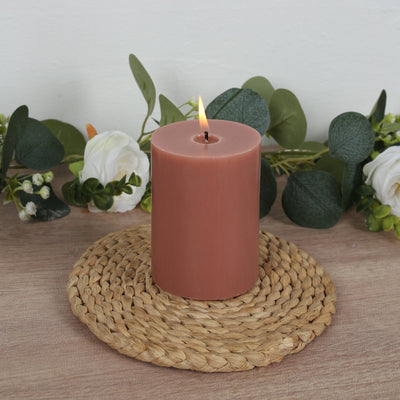 Pink pillar candle on a woven mat with decorative greenery.