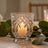 Lit decorative glass candle holder with warm candlelight and eucalyptus leaves
