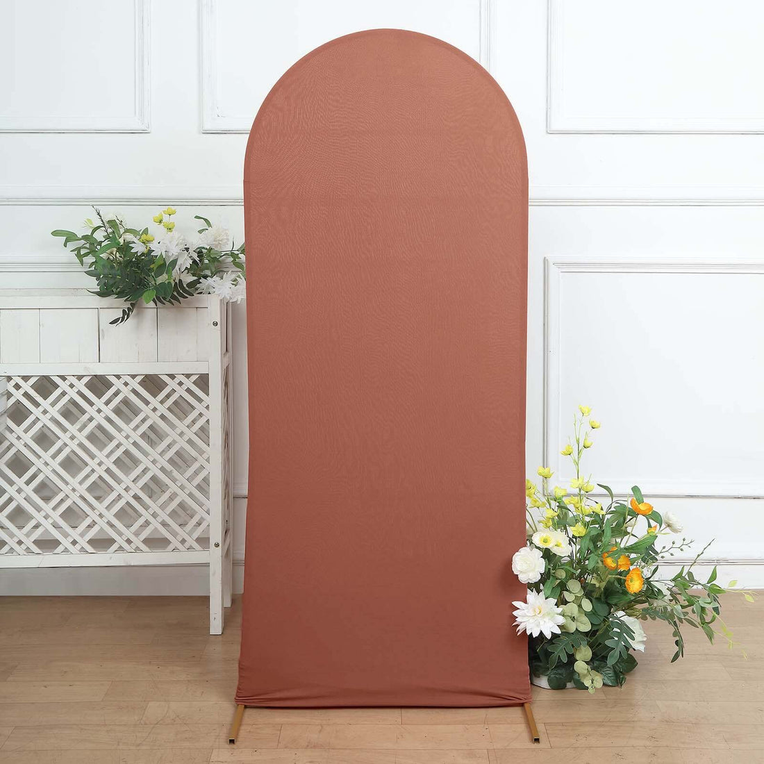 Terra cotta fabric backdrop with a curved top, decorated with flowers and greenery.