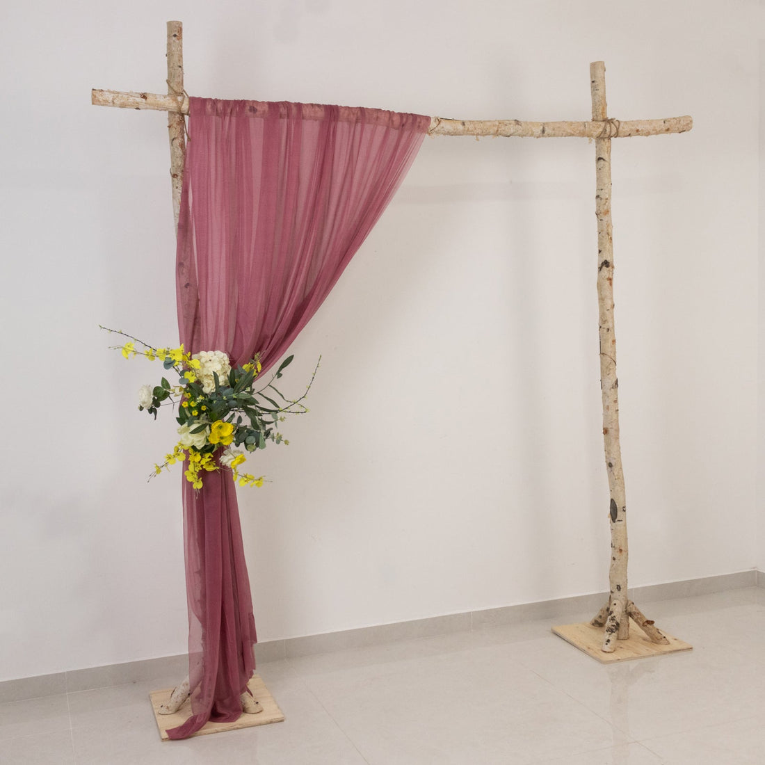 Wooden wedding arch with a burgundy drape and floral arrangement.