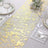 Gold foil table runner on a white table setting with dishes and glassware.
