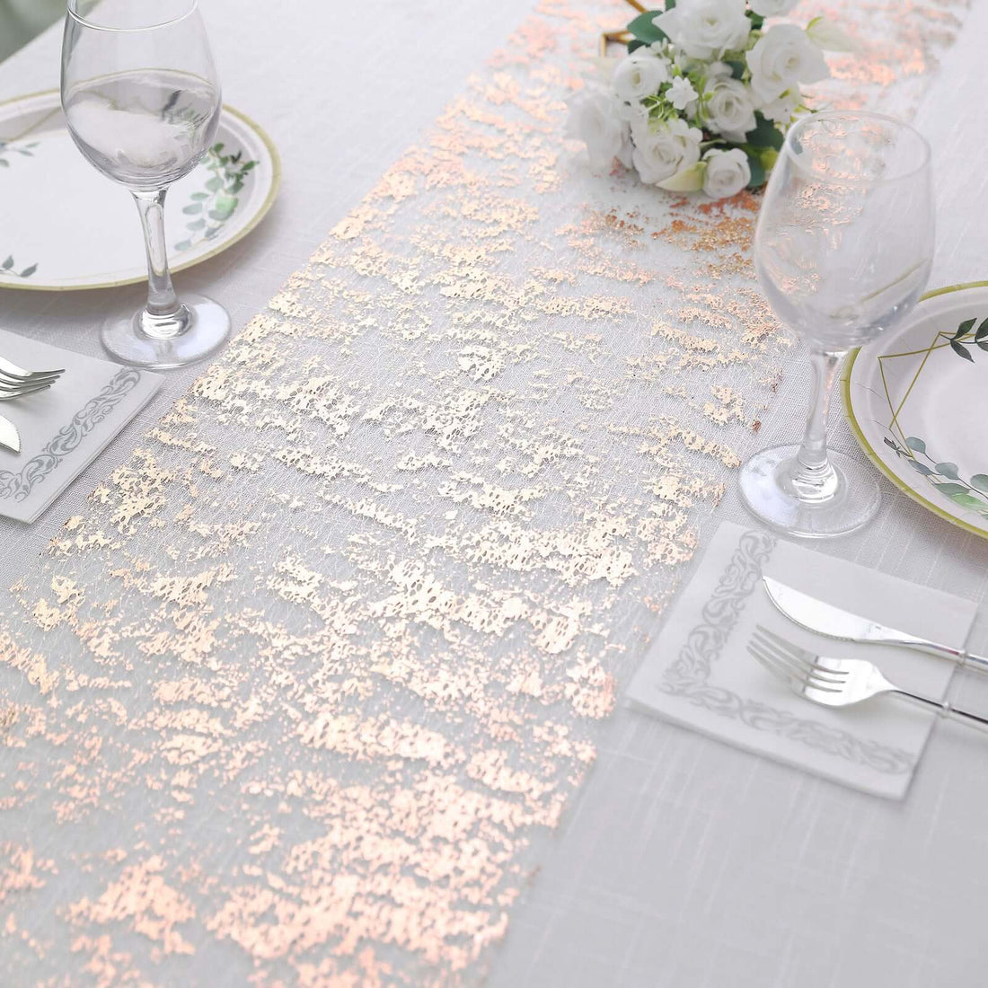 Elegant rose gold table runner on a white table setting with floral decor.