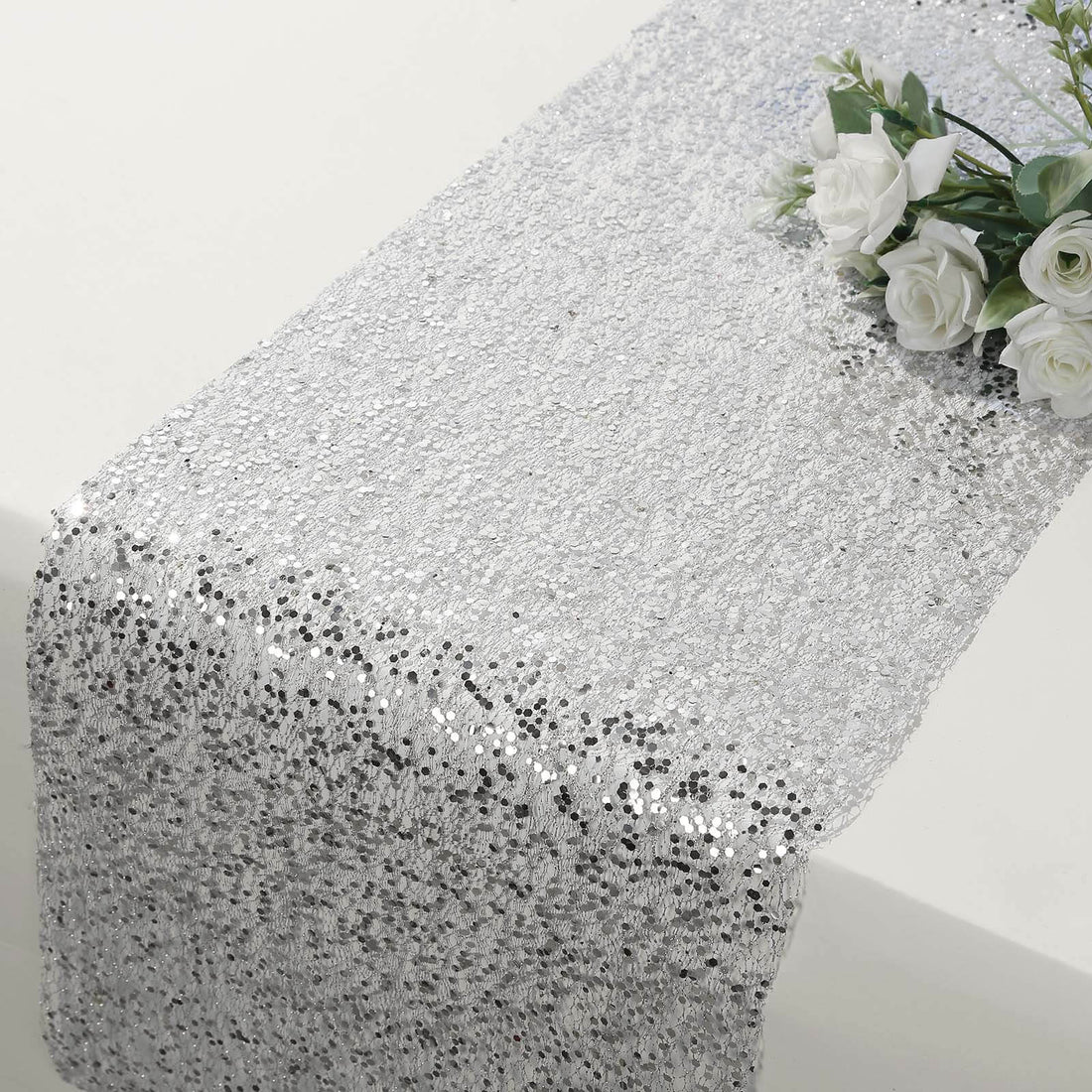 Silver sequin table runner with a floral arrangement on a plain surface